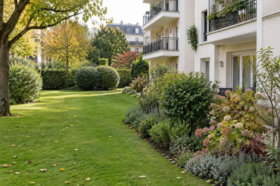 Jardin commun d’une copropriété avec pelouse, haies et massifs entretenus près d’un immeuble résidentiel.